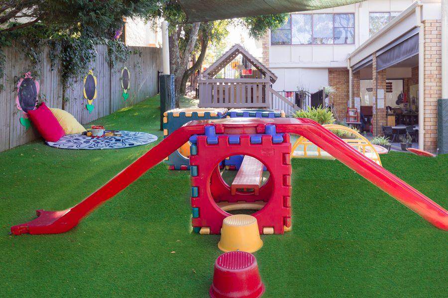 Outdoor playground with cube tunnels, red slide and bright cushions on the artificial grass