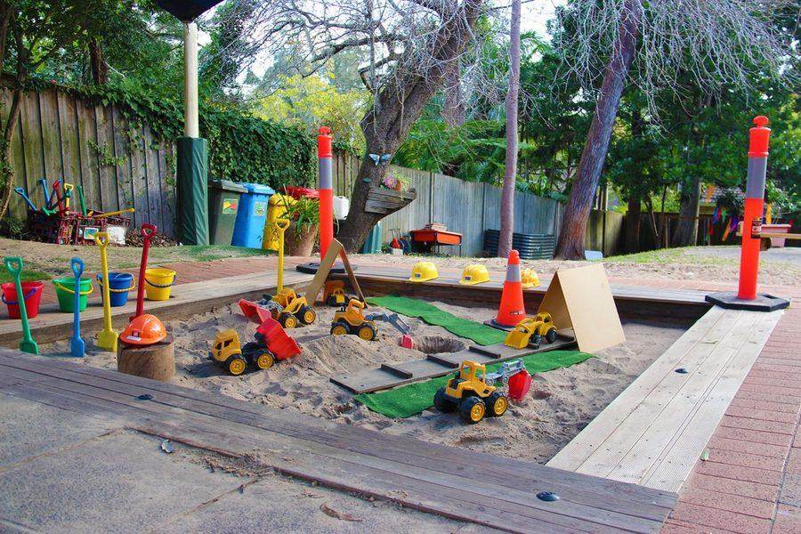 Sandpit with diggers, trucks, traffic cones and gardening tools, set up for construction-themed play