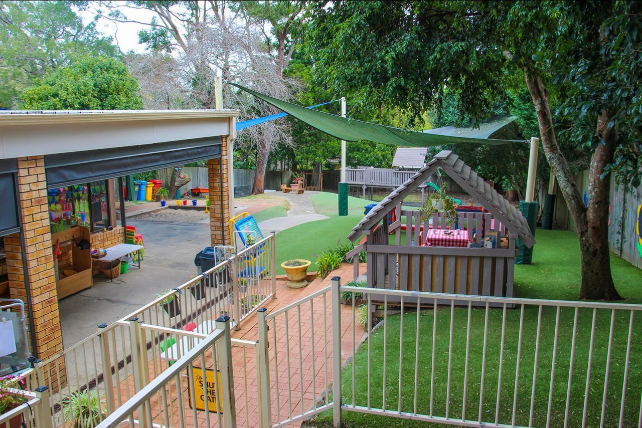 The St Ives Chase Kindergarten outdoor area with cubby, sandpit, garden beds and shade sails under mature gum trees