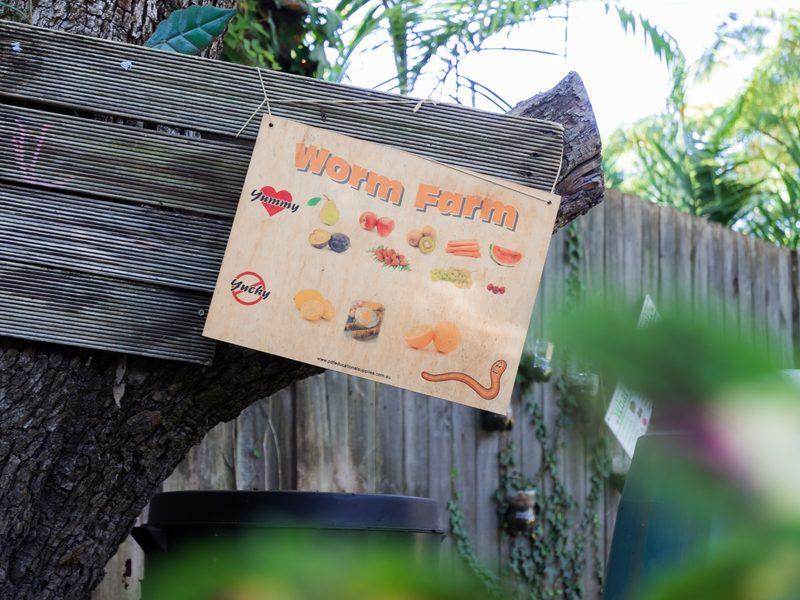 A wooden Worm Farm sign hanging on a tree, listing what worms like to eat
