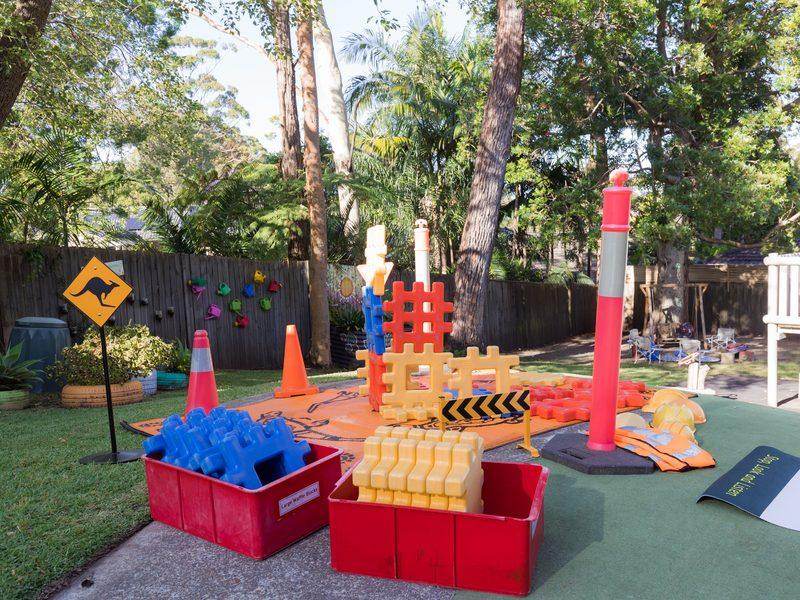 Outdoor construction zone with traffic cones, large waffle building blocks, hi-vis vests and an indigenous-print mat